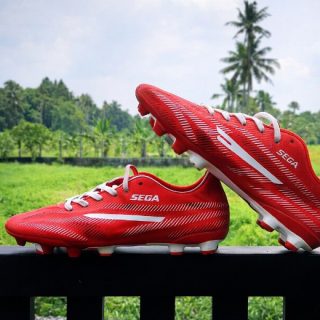 Red Sega Star football boots with white studs on a green background. 1